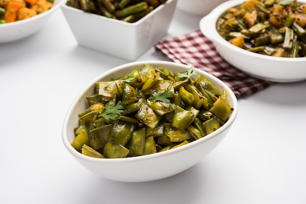 Fried vegetable dish called Flat Green Beans with spices, served in a ceramic bowl, over moody background. selective focus