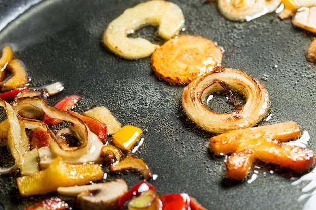 Fried vegetables in the form of letters on a frying pan in oil