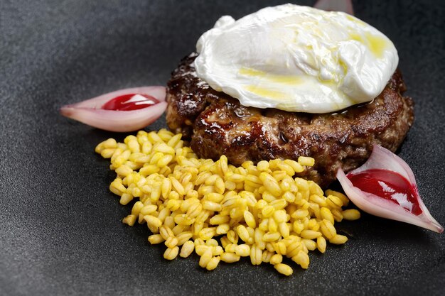 Fried venison steak with poached egg and boiled barley Black isolated background Side view macro