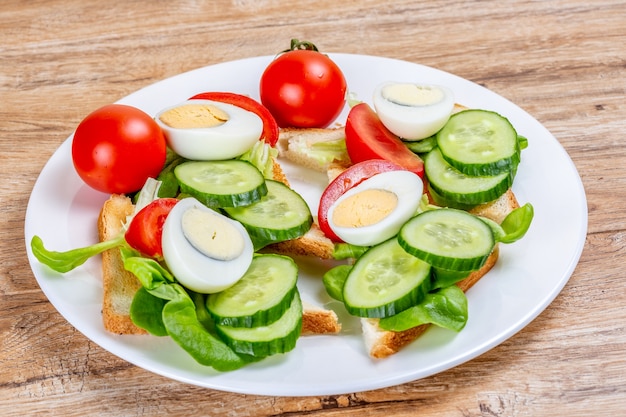 Toast di pane bianco fritto con fette di verdure e uova su un piatto su una superficie di legno