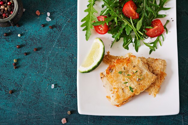 Fried white fish fillets and tomato salad with arugula. top view