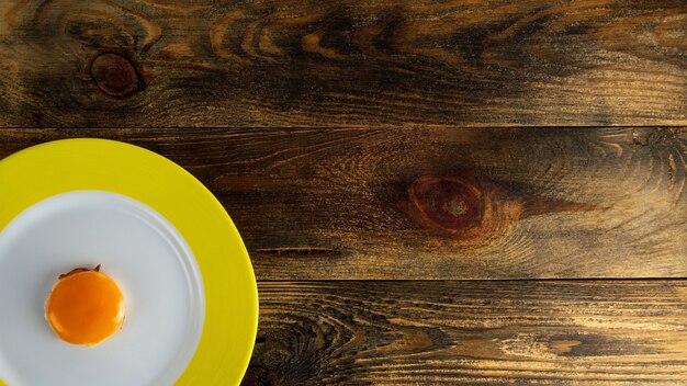 Fried yolk on round ceramic plate with yellow edge on rough wooden surface