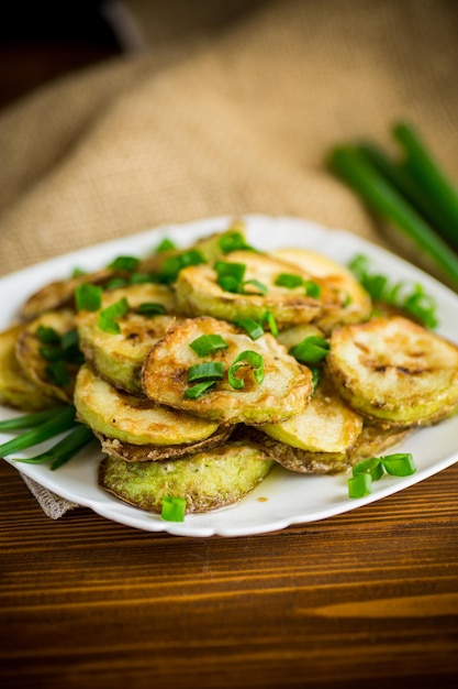 fried zucchini in circles with fresh herbs in a plate on a wooden table