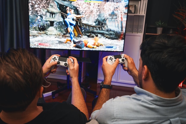 Friend gamers playing video game of battle martial arts fighter on TV using joysticks position of backside background Comfy living neon light at home place with cheerful fighting winner Sellable