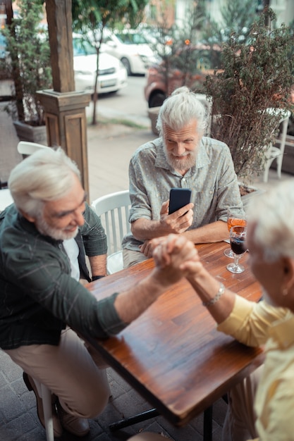 Friend making video. Top view of retired men arm-wrestling while friend making video