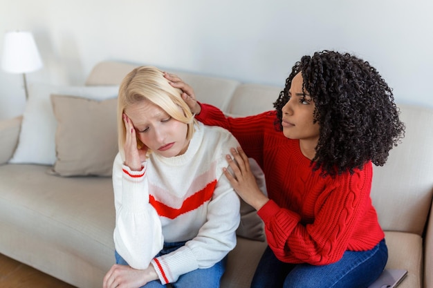 Friend trying to calm down her friend Woman crying Young lady sharing her problem with friend female in depression Woman omforting hes sad friend sitting on a couch in the living room at home