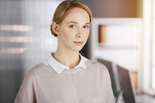 Friendly adult casual dressed business woman standing straight in sunny office. Business headshot