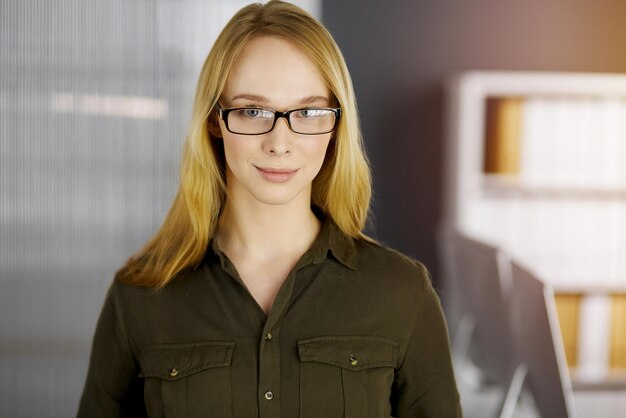 Friendly adult casual dressed business woman standing straight in sunny office. Business headshot.