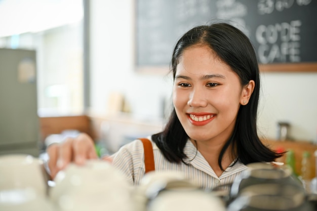 Friendly Asian female coffee shop staff cleaning and adjusting coffee cup on a counter