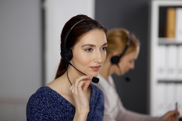 Friendly asian or Latin american businesswoman talking by headset in office. Call center and diverse people group in business.