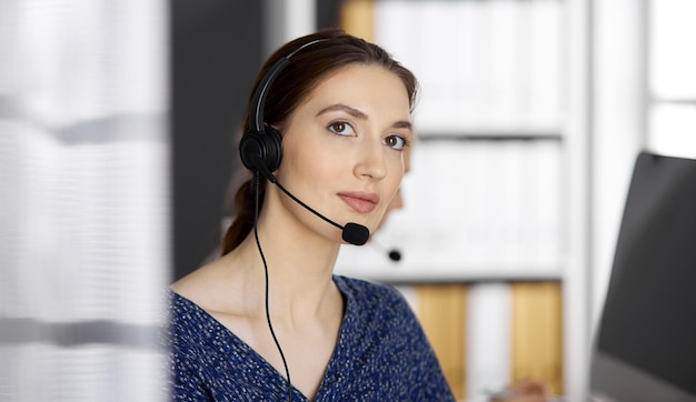 Friendly asian or Latin american businesswoman talking by headset in office. Call center and diverse people group in business.