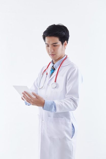 A friendly Asian male doctor in a white coat and red stethoscope using a tablet