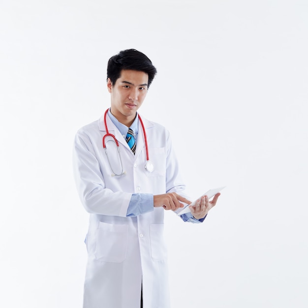 A friendly Asian male doctor in a white coat and red stethoscope using a tablet