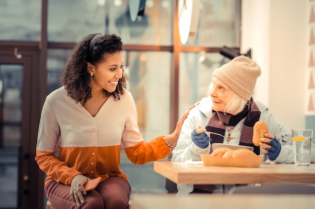 Friendly attitude. joyful friendly woman sitting near her guest while putting a hand on her shoulder