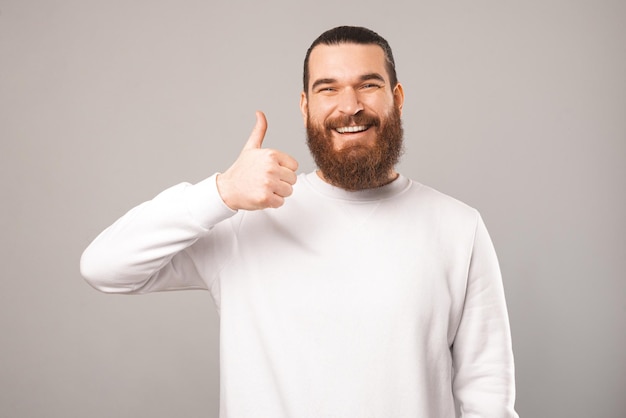 Friendly bearded man is showing thumb up while smiling at the camera