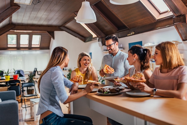 Colleghi amichevoli della squadra di affari che mangiano pizza nell'ufficio coworking.