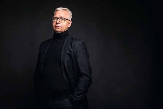 Friendly businessman wearing glasses and a suit posing with smiling at the camera against a black studio background with copy space.