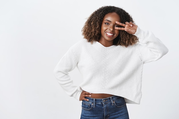 Friendly charming african-american plump young woman shows victory peace gesture near eye