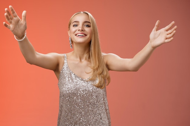 Friendly charming tender hospitable attractive birthday girl in luxury silver dress welcoming guests throw party extend arms cuddle greeting people hug give cuddle smiling broadly red background