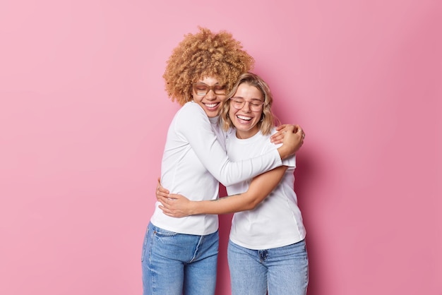 Friendly cheerful optimistic women embrace each other with love and smile gladfully have good relationship feel glad isolated over pink background Friends spend family day together Bonding concept