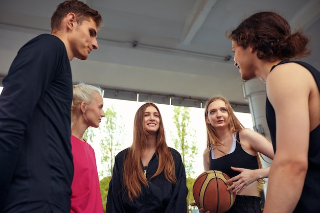 A friendly company of guys and girls are having fun on the basketball court they are going to play