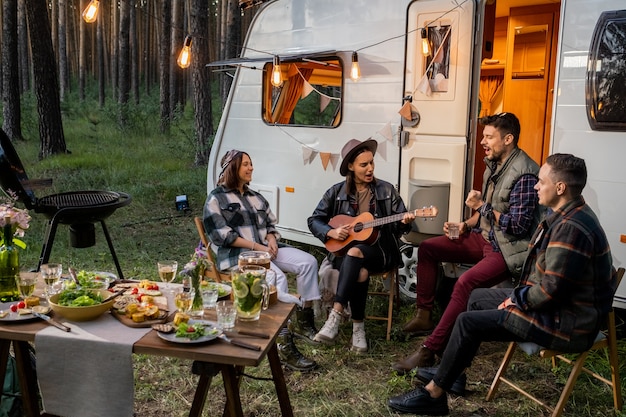 Friendly company sitting by house on wheels and singing songs