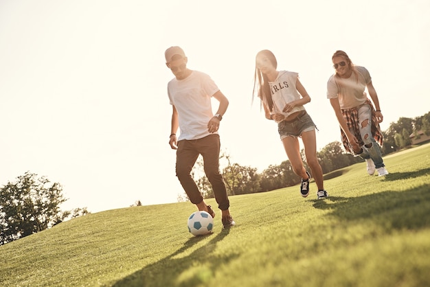 Friendly competition. Full length of happy young people in casual wear running while playing soccer outdoors