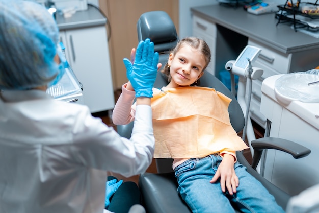 Friendly dentist giving high five little girl sitting on stomatological chair after treatment