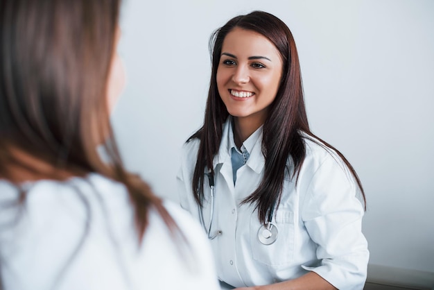 Friendly doctor listening to the patient Young woman have a visit with female doctor in modern clinic