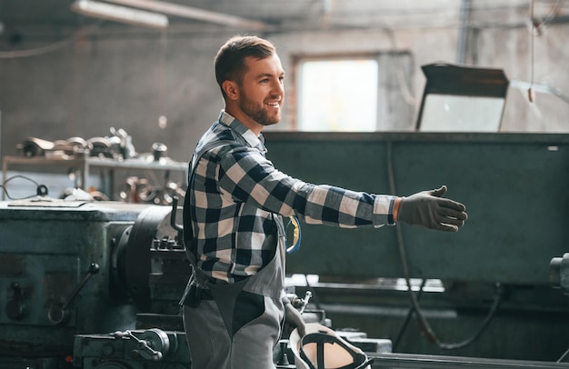 Friendly factory male worker in uniform is indoors giving hand