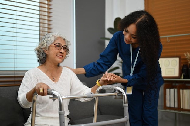 Friendly female caregiver helping elderly woman with walking frame at home Home health care service concept