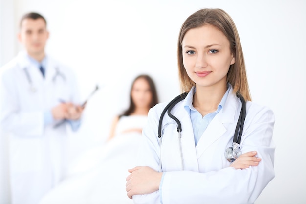 Friendly female doctor on the background with patient in the bed and his physician