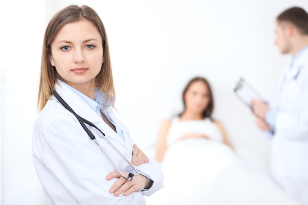 Friendly female doctor on the background with patient in the bed and his physician.