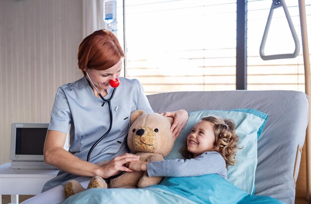 Friendly female doctor examining small girl in bed in hospital