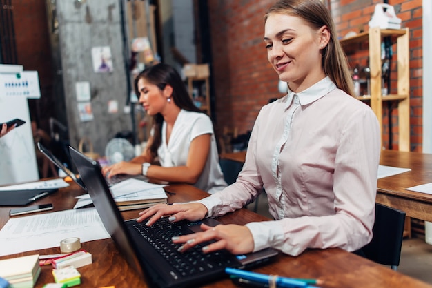 Friendly female office workers wearing formal workwear typing on laptop keyboard working.