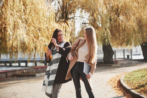 Friendly gesture between these two young and beautiful students in the autumn park