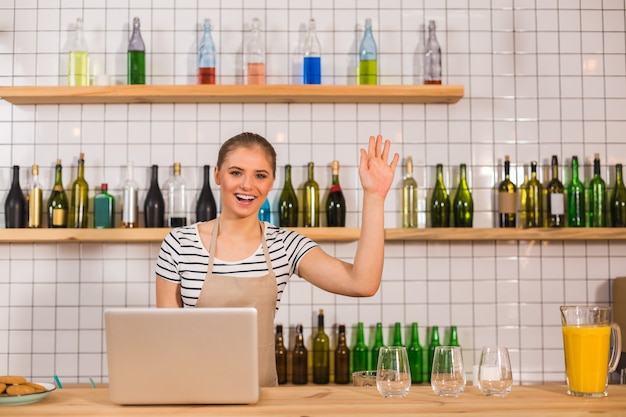 Friendly greeting. Nice delighted friendly woman standing at the counter and waving her hand while greeting a customer