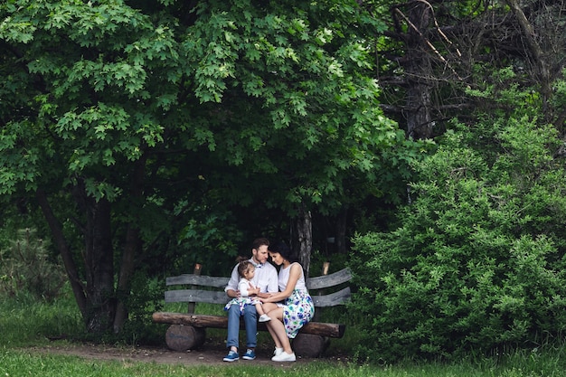 Friendly happy family resting on a wooden bench under the maple.