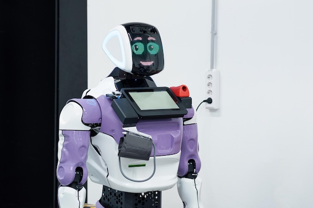 friendly humanoid robot guide expressing emotions is charging from a socket