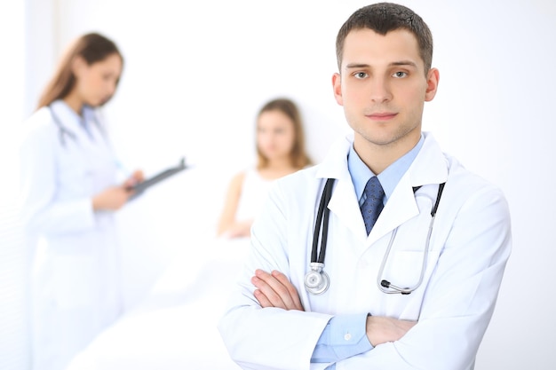 Friendly male doctor on the background with patient in the bed and his physician