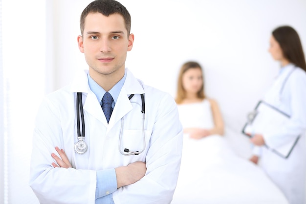 Friendly male doctor on the background with patient in the bed and his physician.