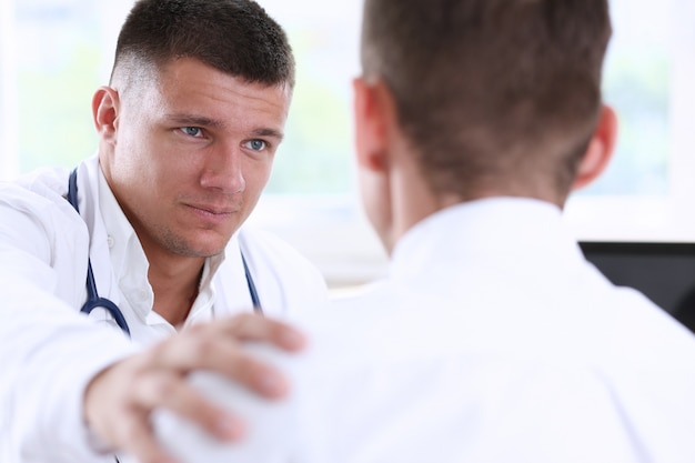 Friendly male doctor hold patient shoulder in office during reception. 