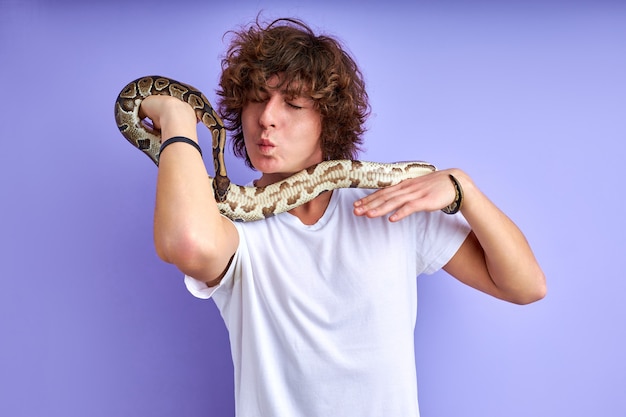 Дружелюбный самец, держащий в руках змею, не боится, никакой фобии. Кавказский мужчина в белой футболке позирует со змеей