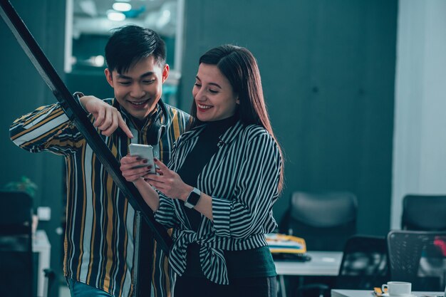 Friendly man and woman standing in the office and looking at the smartphone screen with a smile