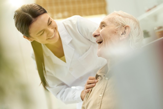 Дружелюбный медик, улыбаясь пожилому человеку, находящемуся на ее попечении