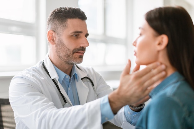 friendly middle aged male doctor checking sore throat or thyroid glands touching neck of young