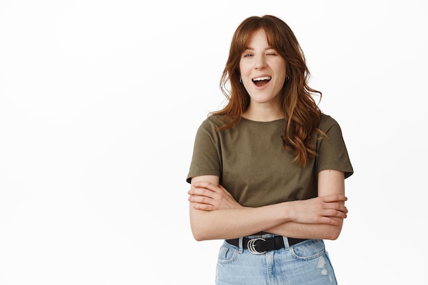 Friendly redhead woman wink at you, smiling and assure all good, everything under control, hinting on some event, standing against white background