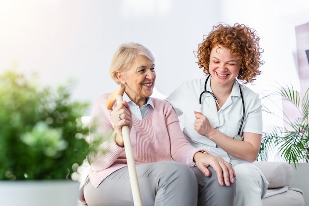 Relazione amichevole tra caregiver sorridente in uniforme e felice donna anziana. giovane infermiera di sostegno che esamina donna senior.