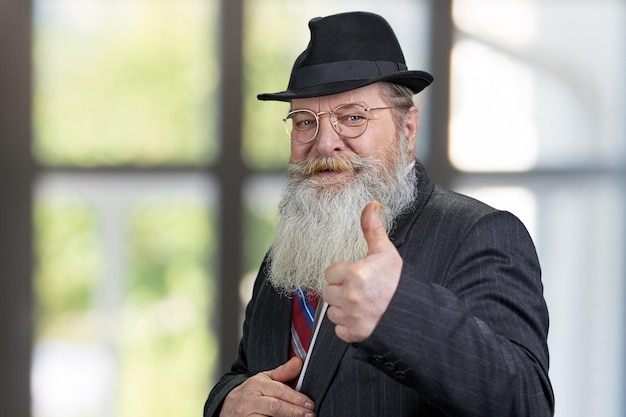 Friendly senior business man with gray beard showing thumb up gesture.