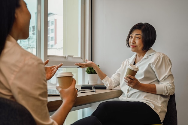 Friendly senior businesswoman talking with younger colleague during coffee break